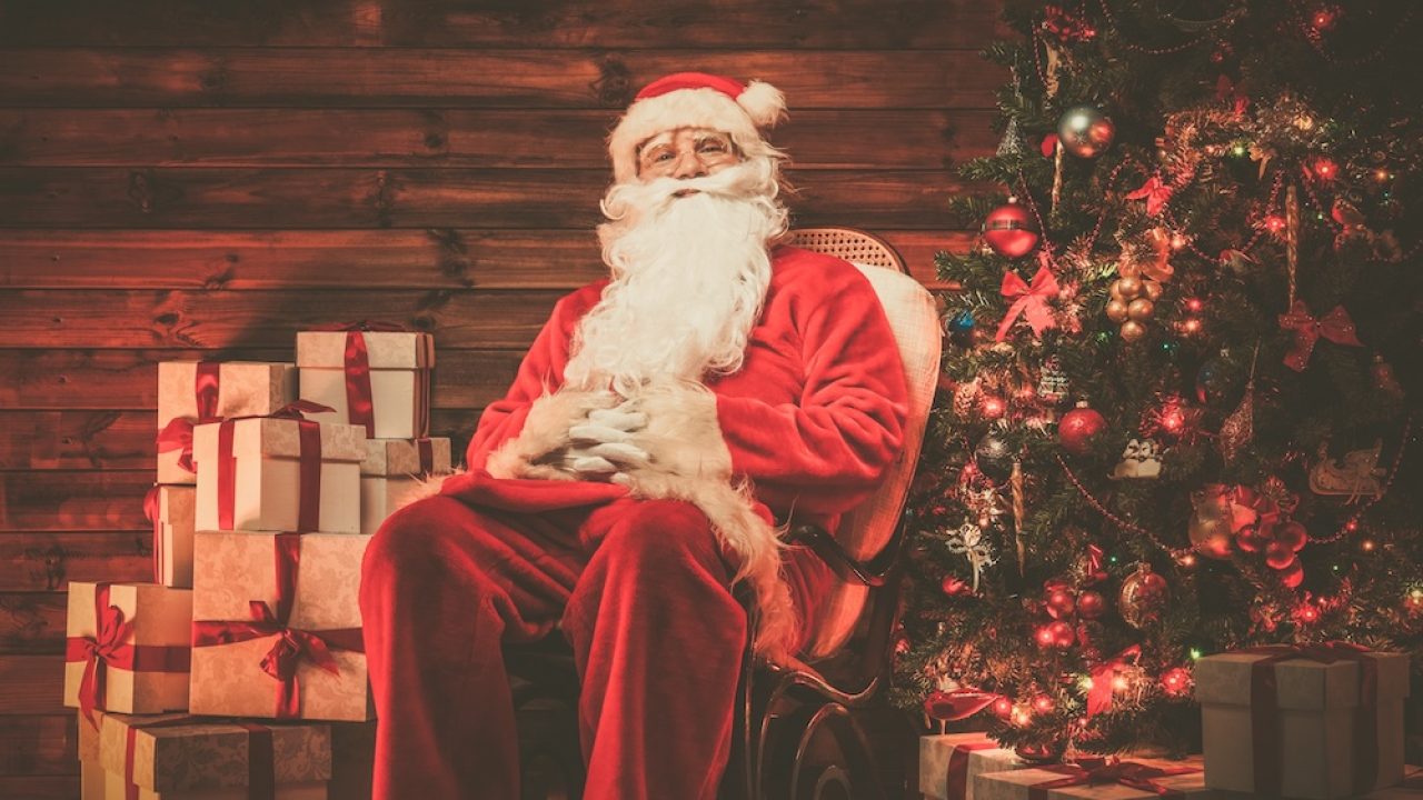 Santa Claus sitting on rocking chair in wooden home interior with gift boxes around him