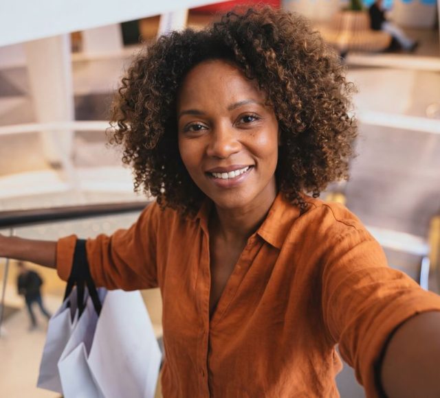 Shoppingläge i kvarteret Utopia. Kvinna med orange blus i rulltrappan med shoppingkassar över armen.