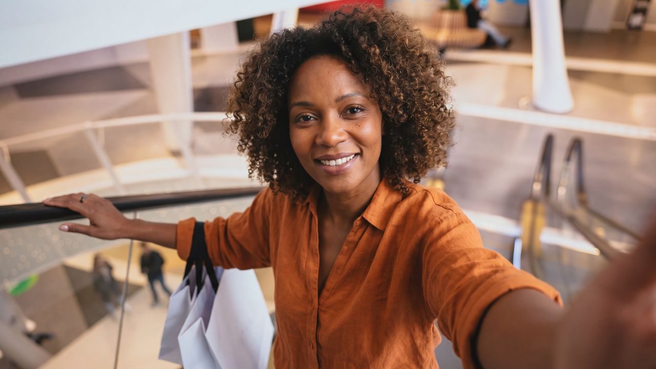 Shoppingläge i kvarteret Utopia. Kvinna med orange blus i rulltrappan med shoppingkassar över armen.