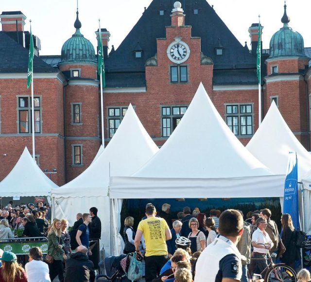 Smakfestivalen i Umeå med stora vita mattält fyllda av besökare framför Umeå stadshus i rött tegel.