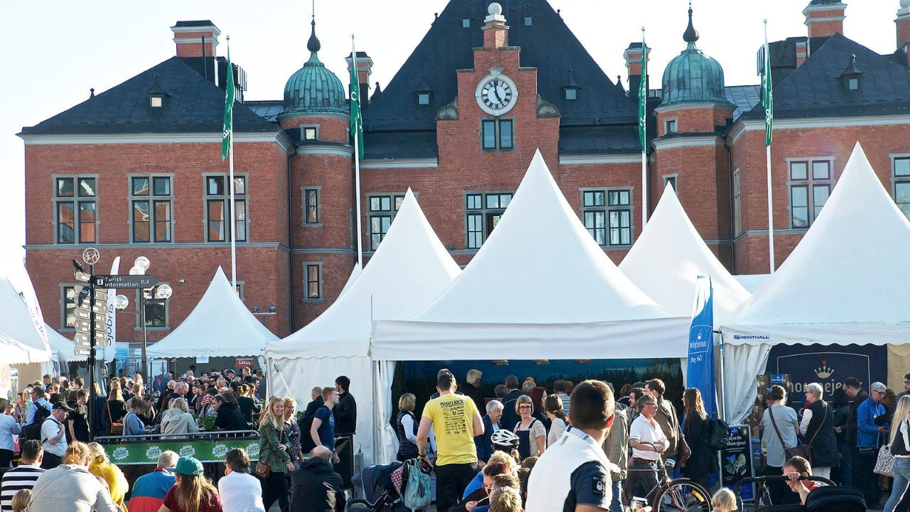 Smakfestivalen i Umeå med stora vita mattält fyllda av besökare framför Umeå stadshus i rött tegel.